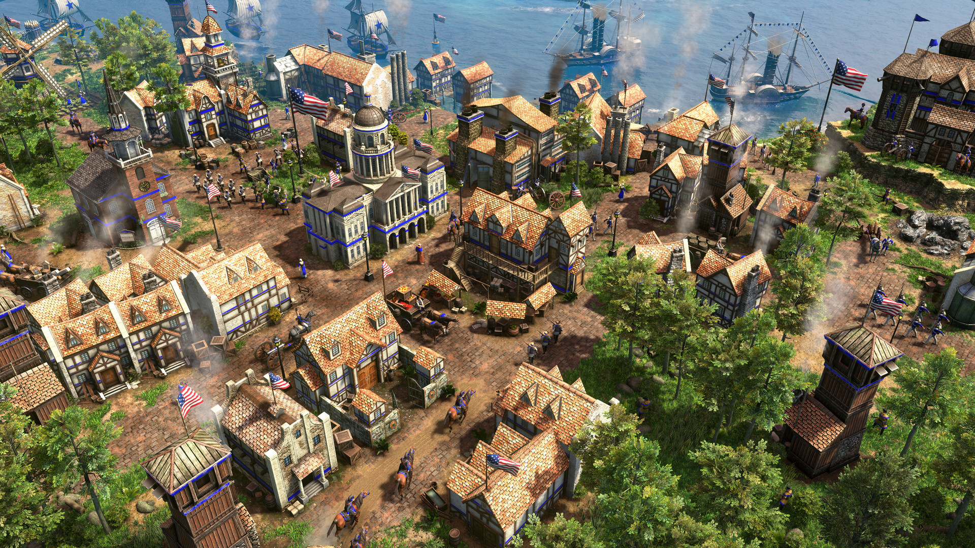 An in-game screenshot of a blue-trimmed city from Age of Empires III: Definitive Edition - United States Civilization. Tall white and tan buildings gather snugly together near a large body of water to the north. Several large ships are traveling along the shore. Patches of trees appear around the outer edges. Several United States flags are placed on random rooftops and on flag poles throughout.